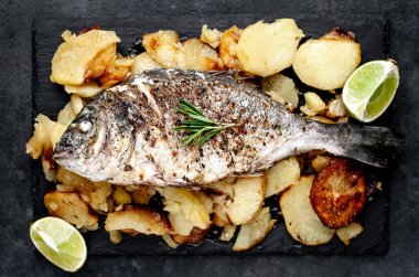 Kayalık zeminde kızarmış Dorado balığı ve patates.