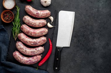 Izgara için çiğ sosis ve arka plandaki kesme tahtasındaki baharatlar.