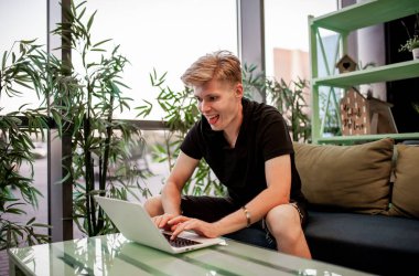Kafeteryadaki masada otururken dizüstü bilgisayarla çalışan genç bir adam.