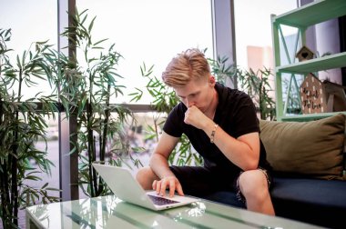 Kafeteryadaki masada otururken dizüstü bilgisayarla çalışan genç bir adam.