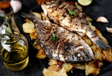 Kayalık zeminde kızarmış Dorado balığı ve patates.