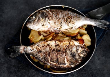 Kayalık zeminde kızarmış Dorado balığı ve patates.