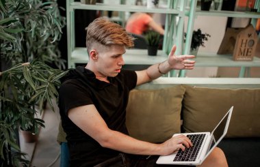 Kafeteryadaki masada otururken dizüstü bilgisayarla çalışan genç bir adam.