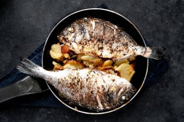 Kayalık zeminde kızarmış Dorado balığı ve patates.