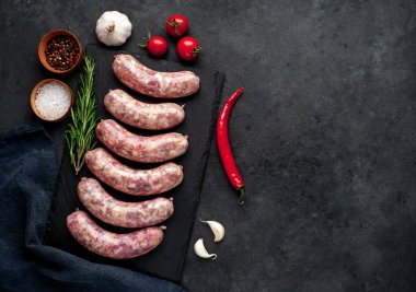 Izgara için çiğ sosis ve arka plandaki kesme tahtasındaki baharatlar.