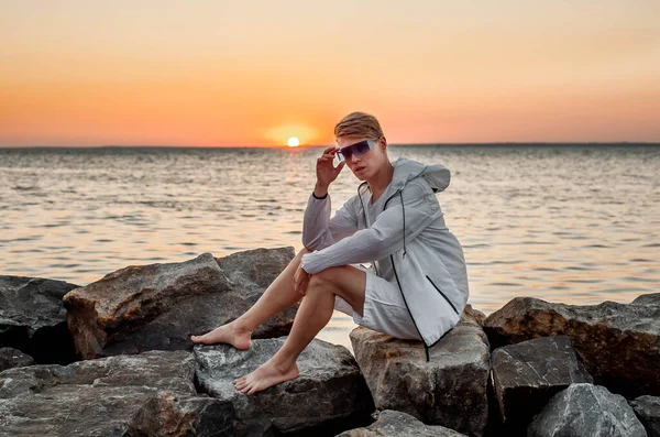 Beyaz elbiseli bir adam deniz kenarında gün batımına bakıyor.