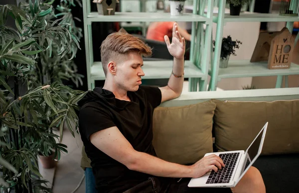 Kafeteryadaki masada otururken dizüstü bilgisayarla çalışan genç bir adam.