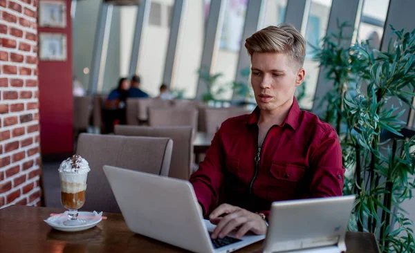 Masada oturan ve dizüstü bilgisayarda çalışan bir adam.