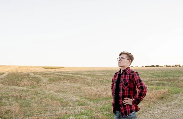 Tişörtlü bir çiftçi gün batımında bir tarlada duruyor.