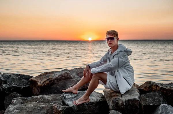 Beyaz elbiseli bir adam deniz kenarında gün batımına bakıyor.