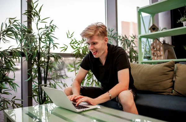 Kafeteryadaki masada otururken dizüstü bilgisayarla çalışan genç bir adam.