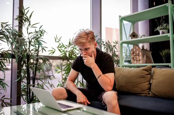 Kafeteryadaki masada otururken dizüstü bilgisayarla çalışan genç bir adam.