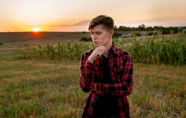 Tişörtlü bir çiftçi gün batımında bir tarlada duruyor.