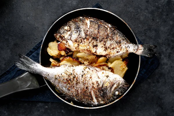 Kayalık zeminde kızarmış Dorado balığı ve patates.