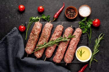 Şişler üzerinde çiğ Lula kebabı ve arka planda baharatlar.