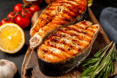 Izgara somon bifteği ve taştan bir arka planda kesim tahtası malzemeleriyle yakın plan görüntüsü.