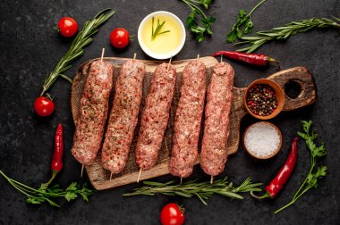 Şiş üzerinde çiğ Lula kebabı ve taş zeminde baharat kesme tahtası.