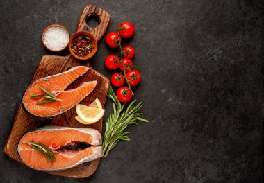 Çiğ balık somon bifteği ve taştan bir arka planda kesim tahtası malzemeleriyle yakın plan görüntüsü.