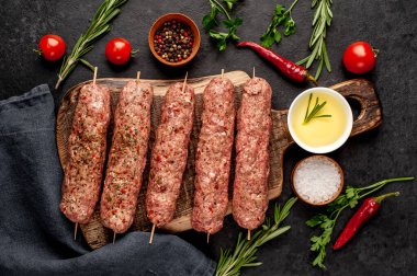 Şiş üzerinde çiğ Lula kebabı ve taş zeminde baharat kesme tahtası.