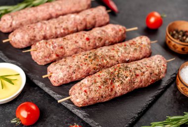 Şişler üzerinde çiğ Lula kebabı ve arka planda baharatlar.