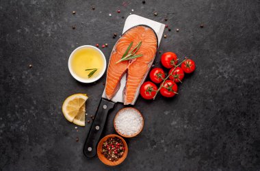 Çiğ balık somon bifteği, arka planda et bıçağının üzerinde malzemeler var.