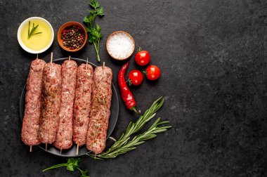 Siyah tabakta baharat ve arka planda taş kaplama şiş üzerinde ham Lula kebabı.