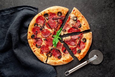 Lezzetli dilimlenmiş sucuklu pizza, salamlı sosis, mozzarella, zeytin, arka planda Provencal otlar.