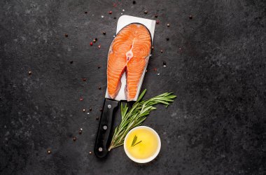 Çiğ balık somon bifteği, arka planda et bıçağının üzerinde malzemeler var.