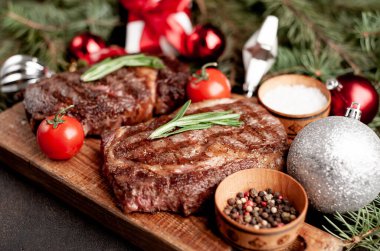 İki kişilik Noel yemeği, ızgara biftek, pirzola, yeşillik ve baharatlar bir taş masanın üzerinde Noel ağacı ve yeni yıl oyuncakları süslemesi.