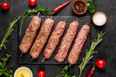 Şişler üzerinde çiğ Lula kebabı ve arka planda baharatlar.