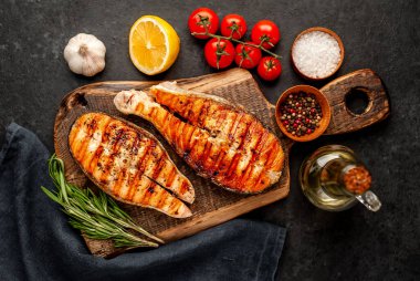 Izgara somon bifteği ve taştan bir arka planda kesim tahtası malzemeleriyle yakın plan görüntüsü.