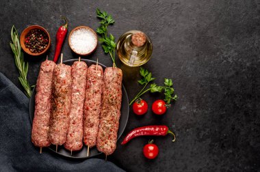 Siyah tabakta baharat ve arka planda taş kaplama şiş üzerinde ham Lula kebabı.