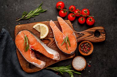 Çiğ balık somon bifteği ve taştan bir arka planda kesim tahtası malzemeleriyle yakın plan görüntüsü.