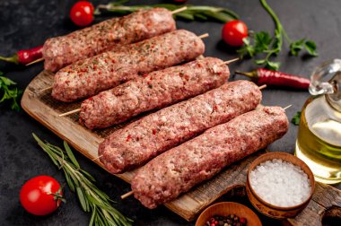 Şiş üzerinde çiğ Lula kebabı ve taş zeminde baharat kesme tahtası.