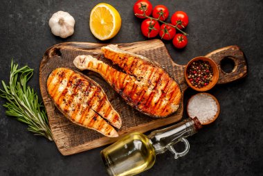 Izgara somon bifteği ve taştan bir arka planda kesim tahtası malzemeleriyle yakın plan görüntüsü.