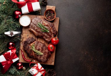 İki kişilik Noel yemeği, ızgara biftek, pirzola, yeşillik ve baharatlar bir taş masanın üzerinde Noel ağacı ve yeni yıl oyuncakları süslemesi.
