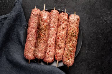 Siyah tabakta baharat ve arka planda taş kaplama şiş üzerinde ham Lula kebabı.