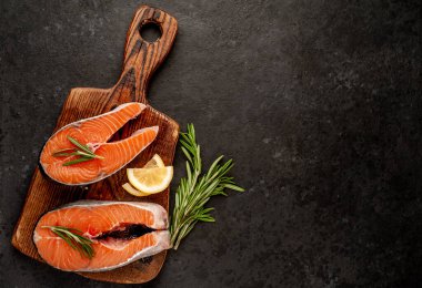 Çiğ balık somon bifteği ve taştan bir arka planda kesim tahtası malzemeleriyle yakın plan görüntüsü.