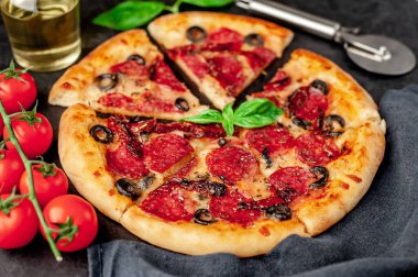 Lezzetli dilimlenmiş sucuklu pizza, salamlı sosis, mozzarella, zeytin, arka planda Provencal otlar.