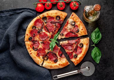 Lezzetli dilimlenmiş sucuklu pizza, salamlı sosis, mozzarella, zeytin, arka planda Provencal otlar.