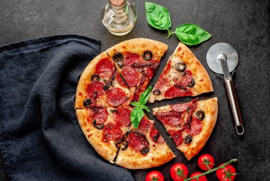 Lezzetli dilimlenmiş sucuklu pizza, salamlı sosis, mozzarella, zeytin, arka planda Provencal otlar.