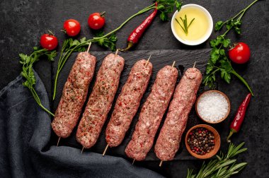 Şişler üzerinde çiğ Lula kebabı ve arka planda baharatlar.