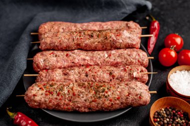 Siyah tabakta baharat ve arka planda taş kaplama şiş üzerinde ham Lula kebabı.