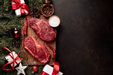 Noel tatili için iki kişilik yemek hazırlamak için çiğ pirzola bifteği ve Noel ağacı ve süslemeleri olan taş bir masada.