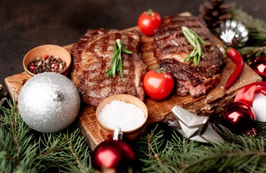 İki kişilik Noel yemeği, ızgara biftek, pirzola, yeşillik ve baharatlar bir taş masanın üzerinde Noel ağacı ve yeni yıl oyuncakları süslemesi.