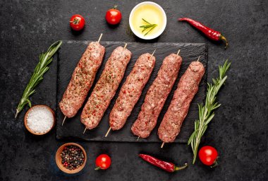 Şişler üzerinde çiğ Lula kebabı ve arka planda baharatlar.