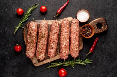 Şiş üzerinde çiğ Lula kebabı ve taş zeminde baharat kesme tahtası.