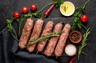 Şişler üzerinde çiğ Lula kebabı ve arka planda baharatlar.