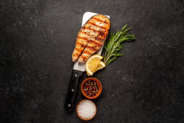 Izgara somon bifteği, arka planda et bıçağının üzerinde malzemeler var.