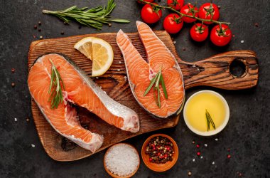 Çiğ balık somon bifteği ve taştan bir arka planda kesim tahtası malzemeleriyle yakın plan görüntüsü.